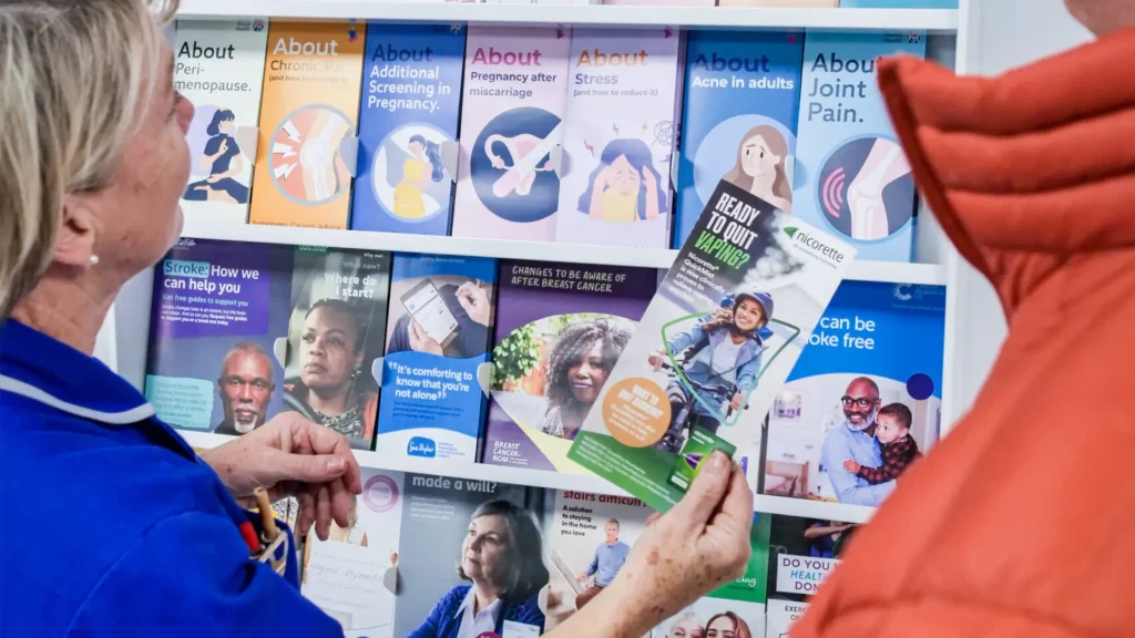 Two people in a GP reception looking at the leaflets
